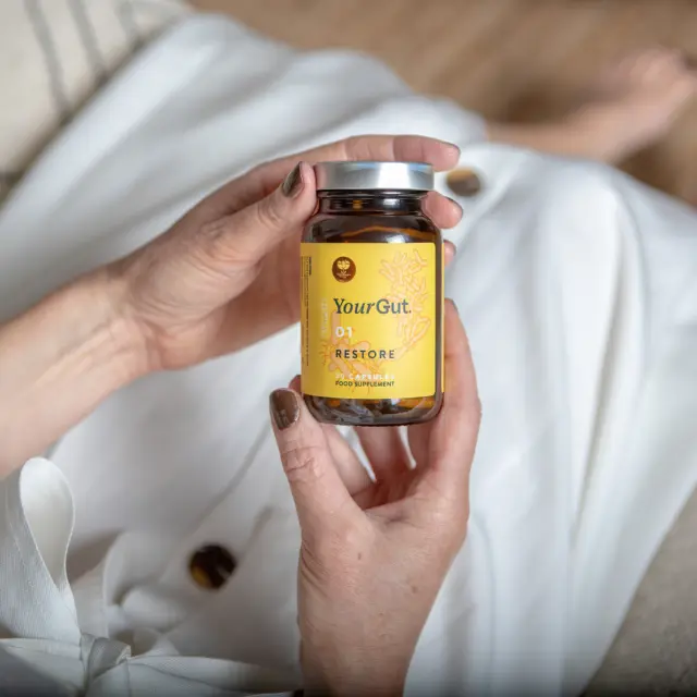 Hands holding a jar of YourGut 01 Restore food supplement capsules.