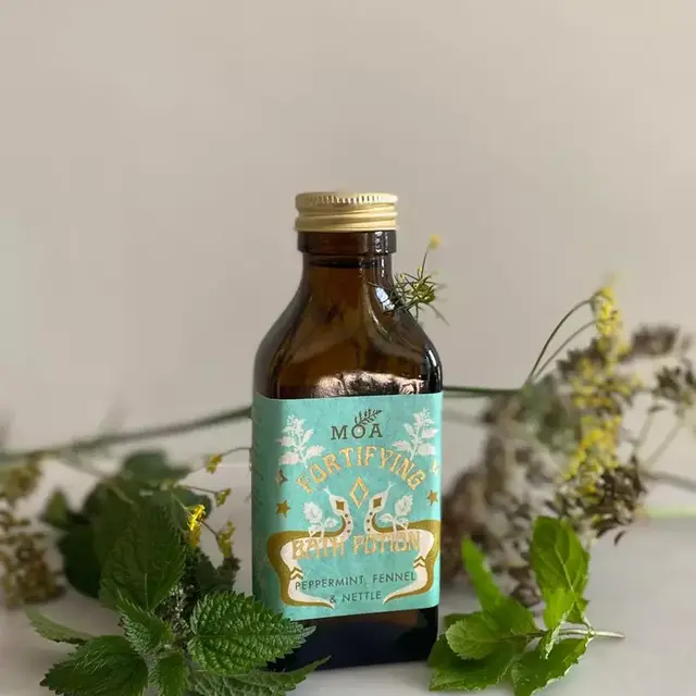 Brown bottle with blue label, "MOA Fortifying Green Potion", surrounded by herbs.
