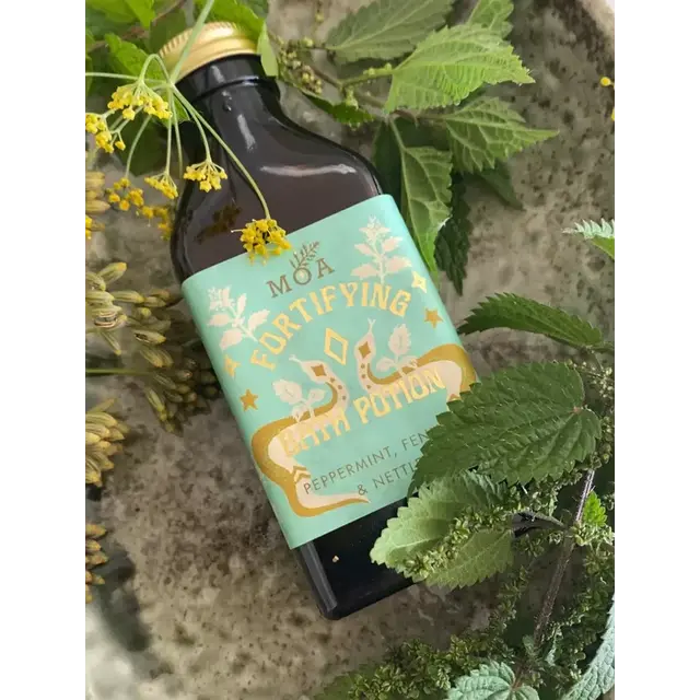 Fortifying bath potion bottle with peppermint, fennel, and nettle, surrounded by green leaves.