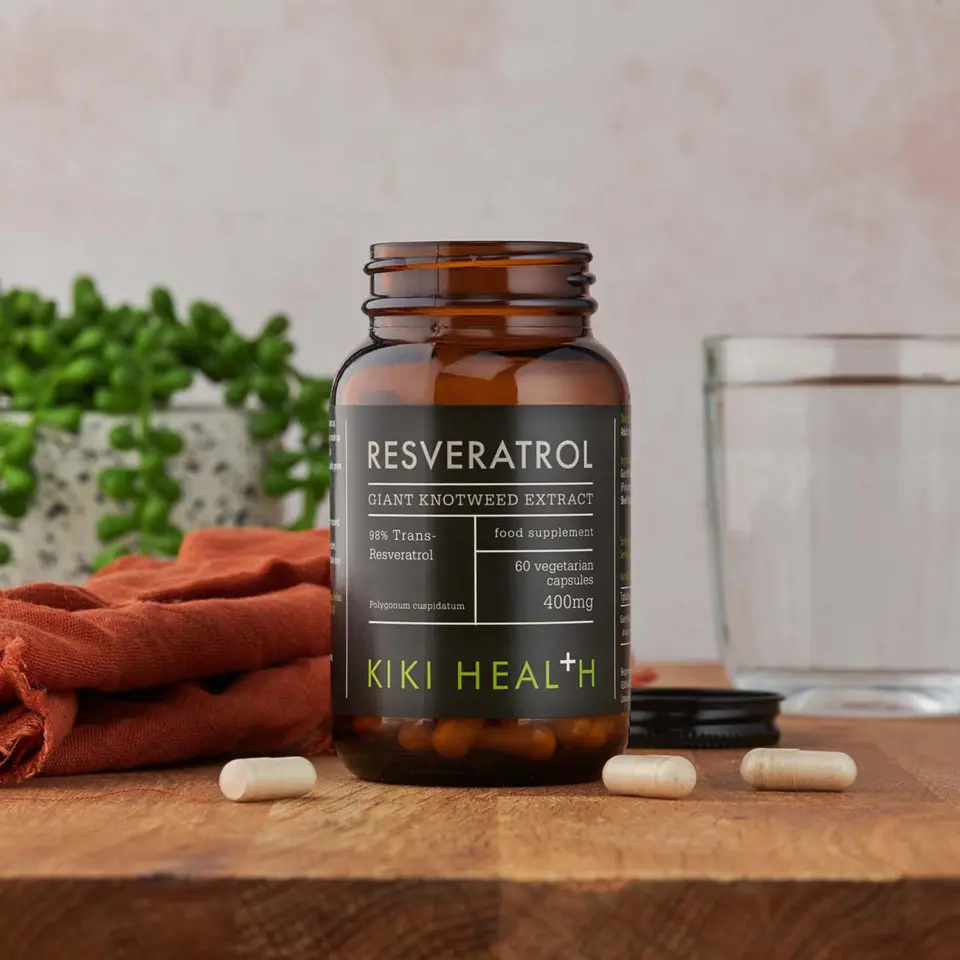 Kiki Health Resveratrol supplement bottle on wooden table with capsules and glass.