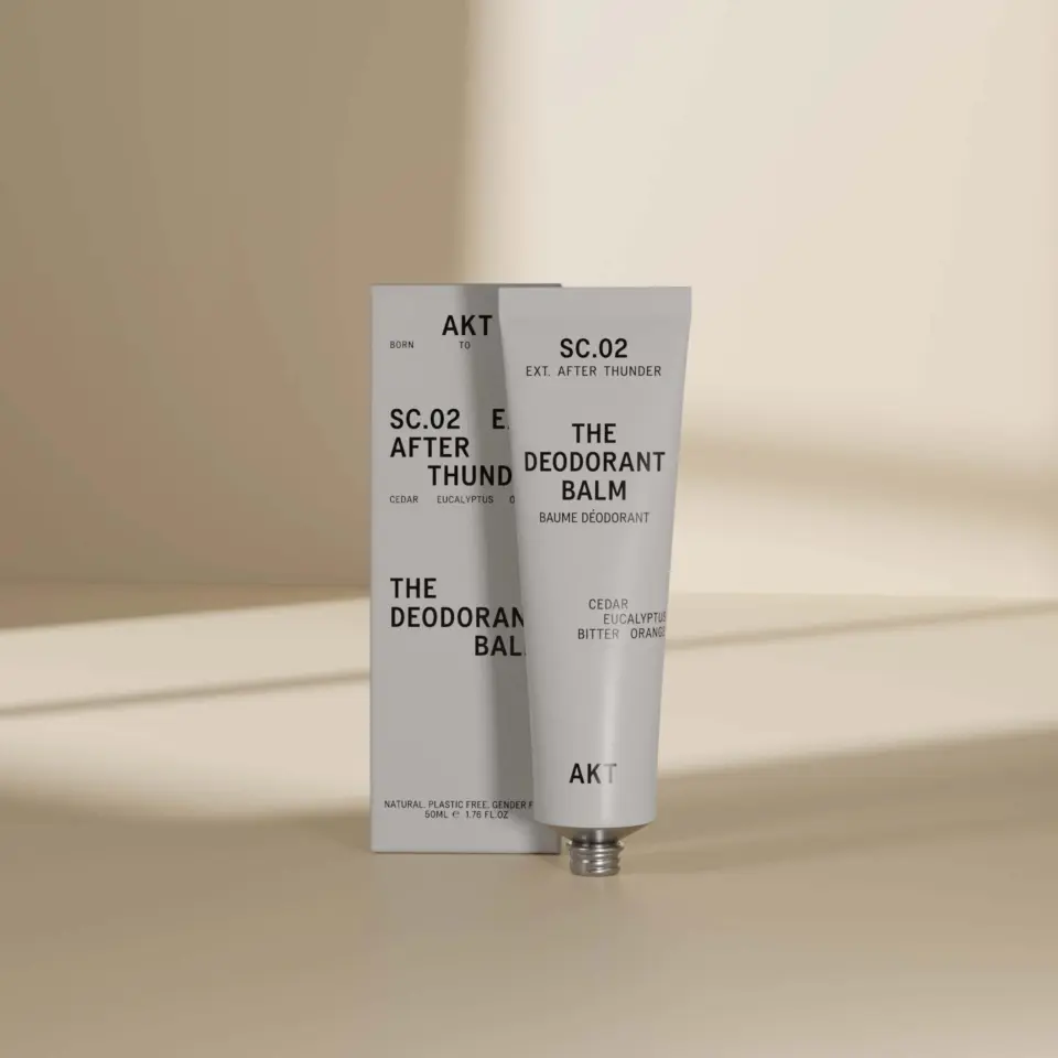 AKT SC.02 After Thunder deodorant balm tube and box on a beige surface.