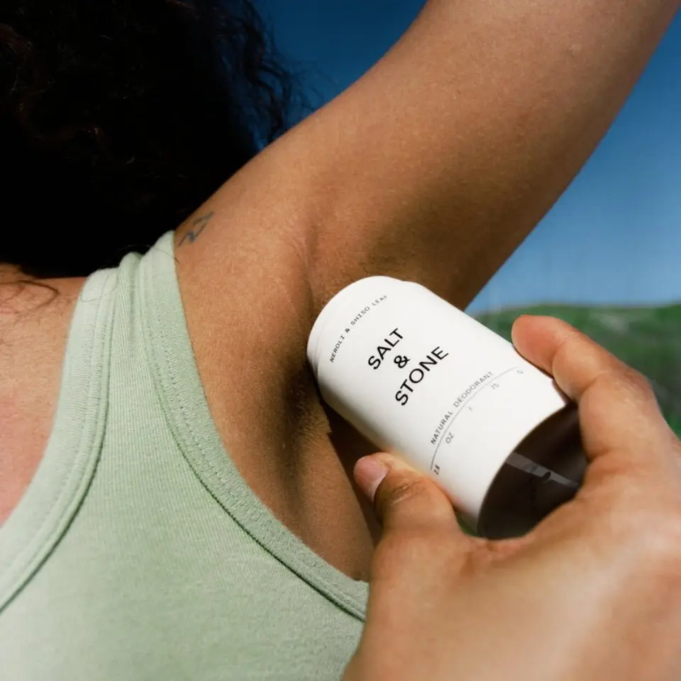 Person applying Salt & Stone deodorant to armpit outdoors.