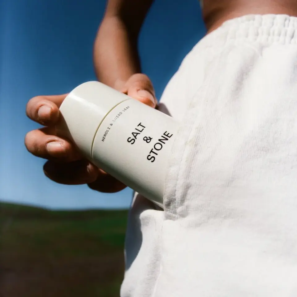 Person holding Salt & Stone deodorant against white trousers outdoors.