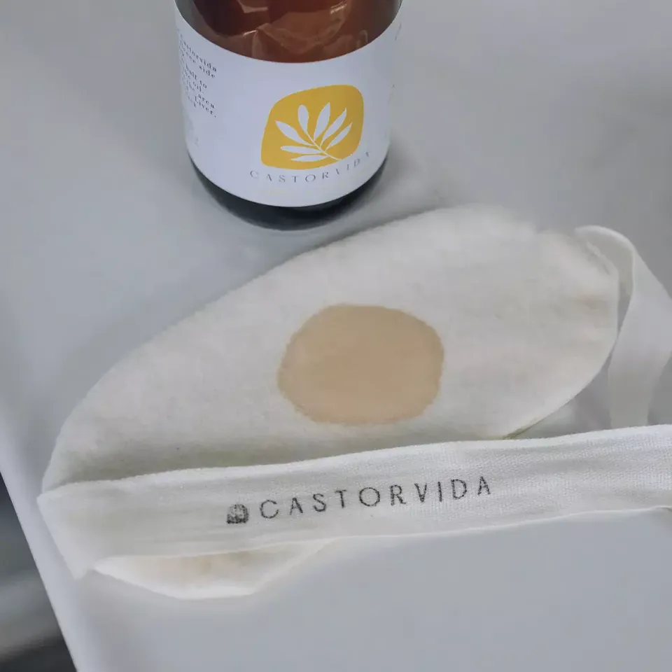 Bottle with Castorvida label and a fabric pad with a stain on a white surface.
