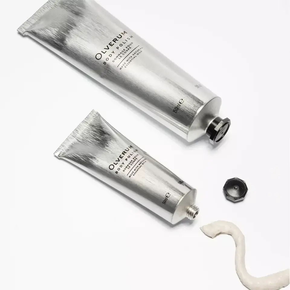 Two silver tubes of Olverum Body Polish on a white background, with cream and a black cap.
