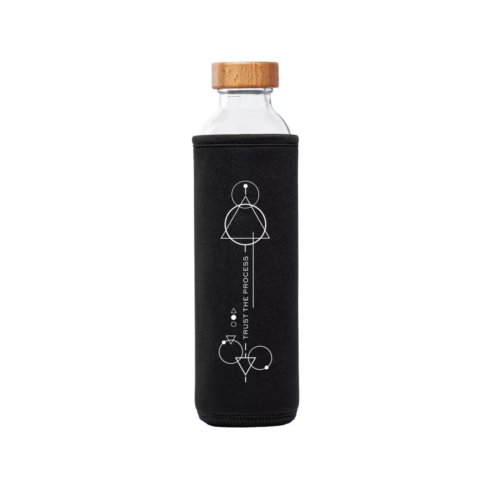 Glass bottle with wooden lid in black sleeve, geometric design, text: "Trust the Process".
