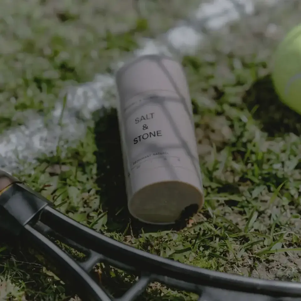 Salt & Stone deodorant on grass beside a tennis racket and ball.
