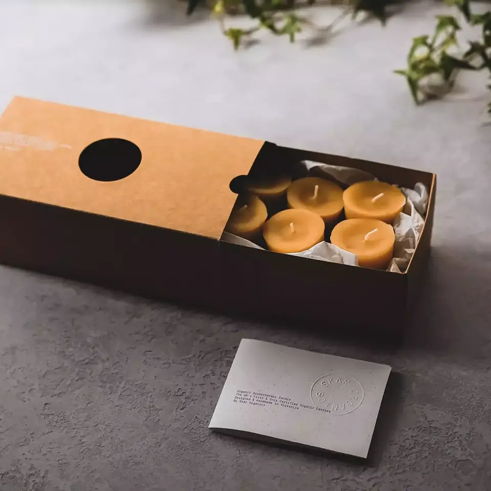 Brown box with six yellow candles, card with embossed text, and green ivy in the background.