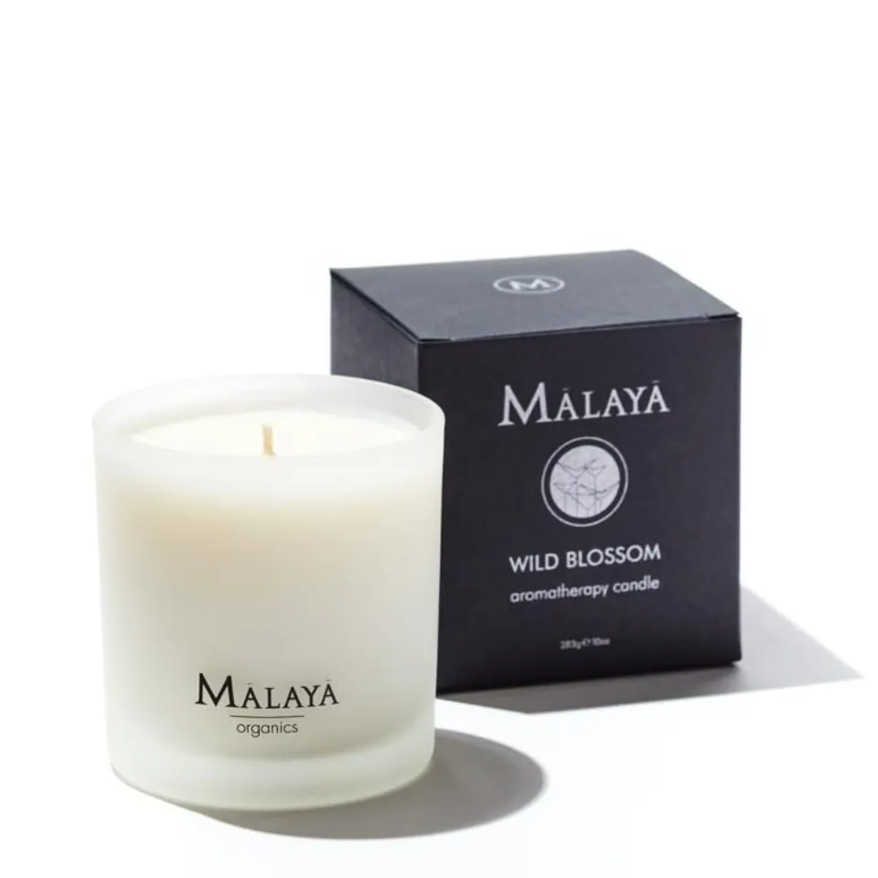 White candle in frosted glass with "Malaya organics" text, next to black box labelled "Wild Blossom".