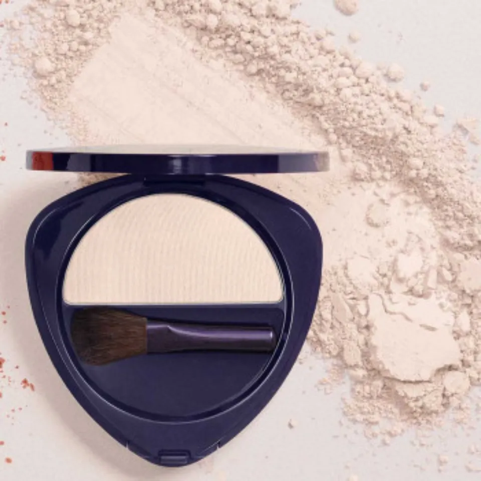 Compact with white powder and brush, surrounded by loose powder.