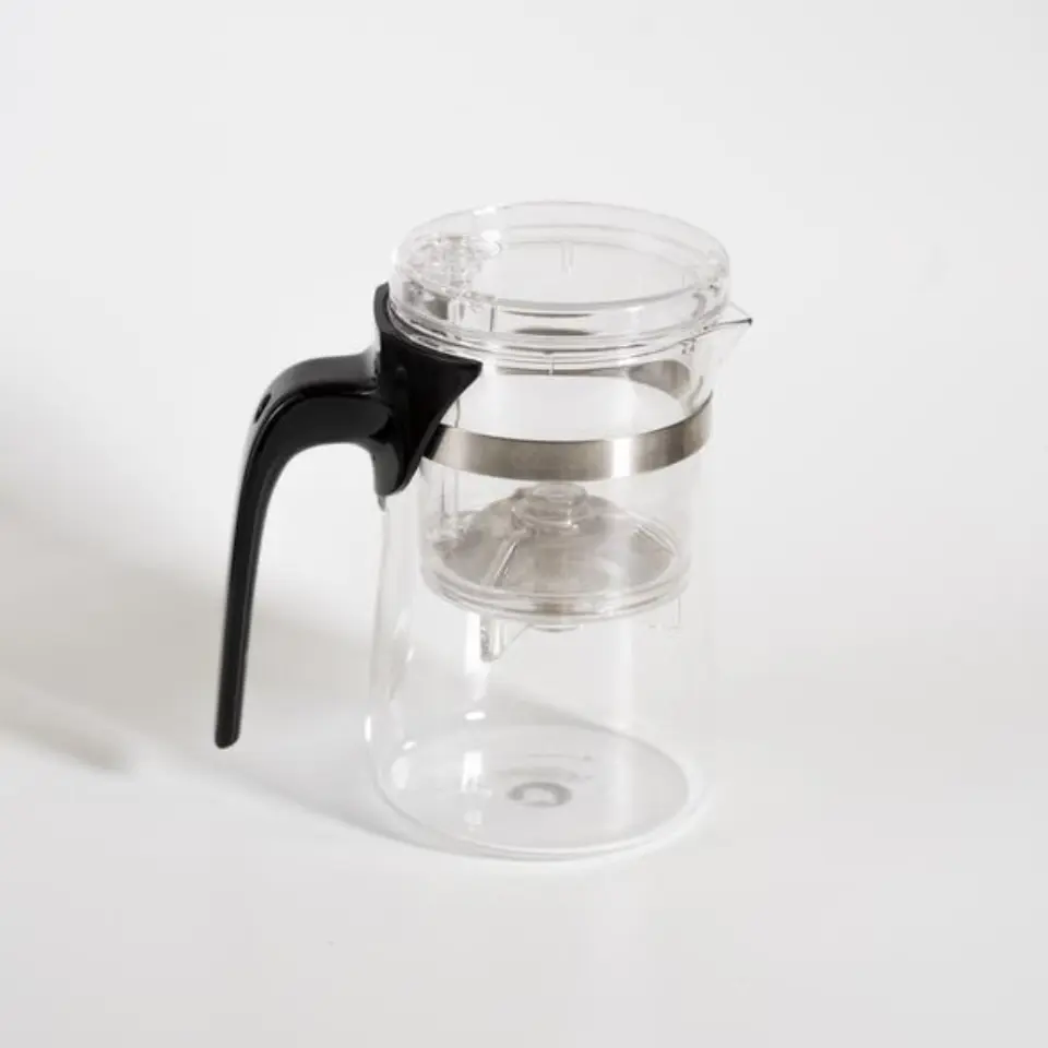 Clear glass teapot with black handle and metal band on white background.