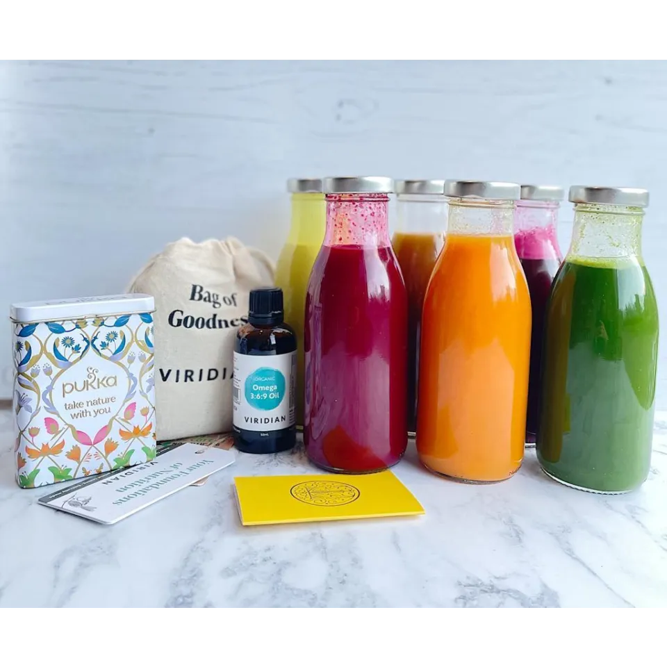 Assorted juice bottles, Viridian Omega oil, Pukka tin, and Bag of Goodness on marble surface.