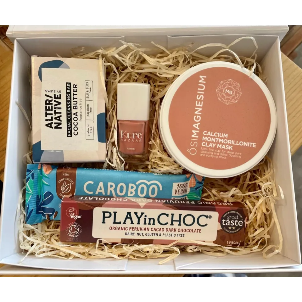 Gift box with clay mask, cleansing bar, nail polish, and vegan chocolate bars on straw filling.