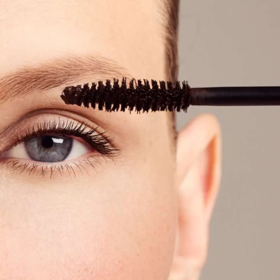 Close-up of a mascara wand near an eye with long lashes.