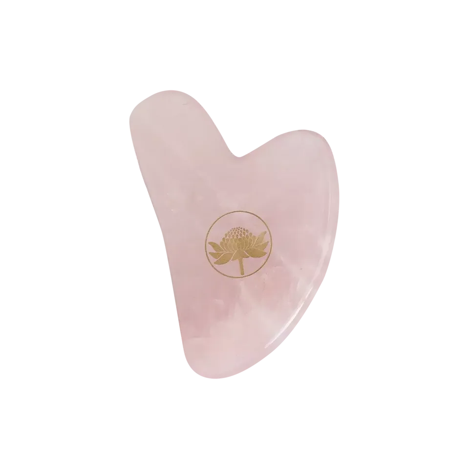 Pink heart-shaped gua sha tool with a gold floral logo.