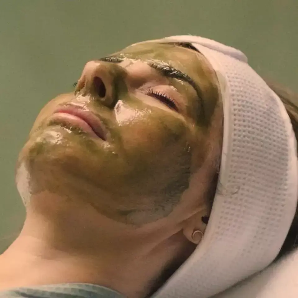 Person with green face mask, eyes closed, wearing a white headband.