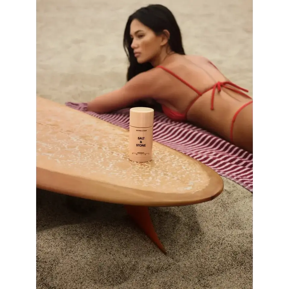Deodorant stick on surfboard, woman in red bikini on sand.