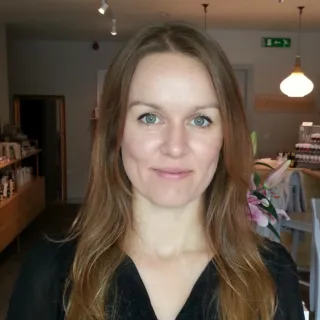 Woman with long hair in a skincare shop, shelves and products visible.