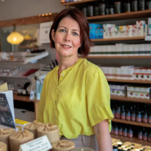 Woman in a yellow shirt standing in a skincare shop with shelves of products behind her.