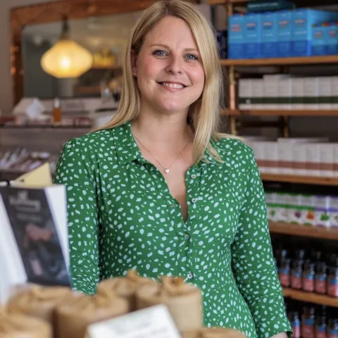 Woman in green blouse in a skincare shop with shelves of products in the background.