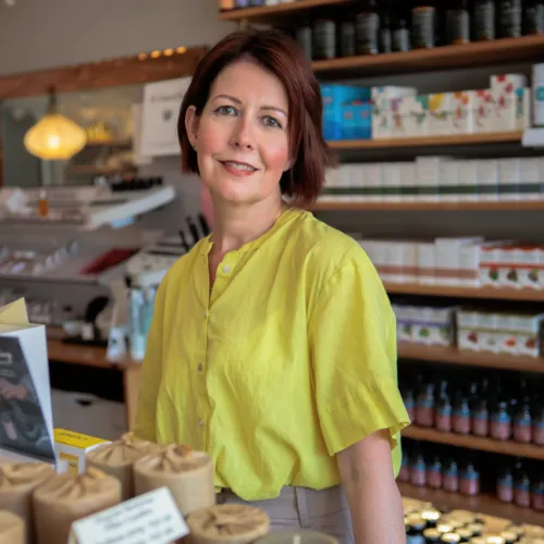 Woman in a yellow shirt standing in a skincare shop with shelves of products behind her.