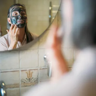 Person applying a black face mask in a bathroom mirror.