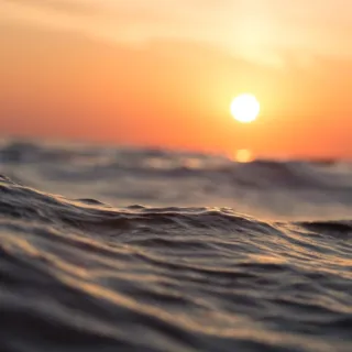Sunset over calm ocean waves with an orange sky.