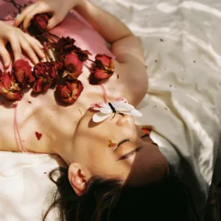 Person lying on a bed with red roses and a butterfly on their face.