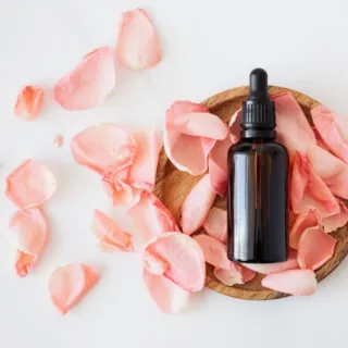 Brown dropper bottle on wooden dish with pink rose petals.