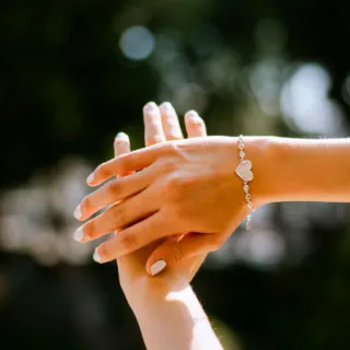 Hands with a silver heart bracelet against a blurred outdoor background.