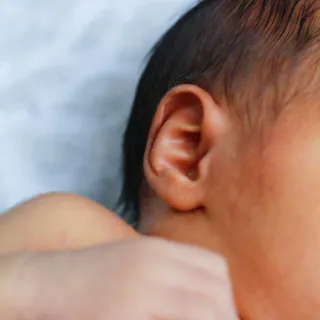 Close-up of a baby's ear and hand resting on a soft white blanket.