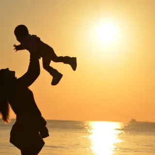 Silhouette of a person lifting a child at sunset by the sea.