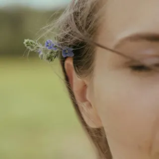 Woman with small purple flowers in hair, outdoors.
