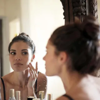 Woman applying skincare cream in front of a mirror.