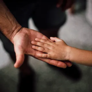 Adult and child hands touching, palm to palm, against a blurred background.