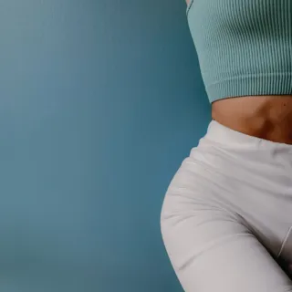 Person in a teal top and white shorts against a blue wall.