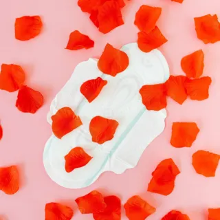 Sanitary pad on pink background with scattered red rose petals.