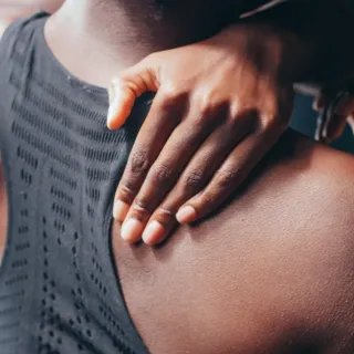 Person touching their shoulder, wearing a sleeveless top.