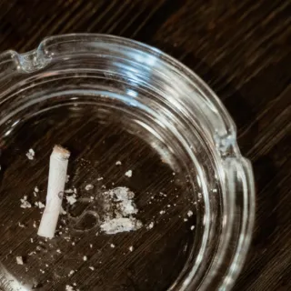 Glass ashtray with cigarette butt and ash on a wooden table.