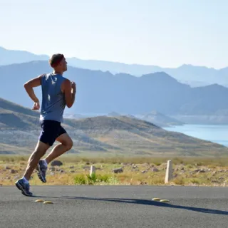 Man running on a road with mountains and a lake in the background.