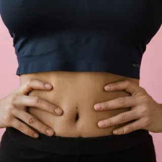 Person in a navy crop top with hands on hips against a pink background.