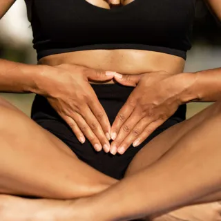 Person in black activewear sitting cross-legged, hands resting on abdomen.