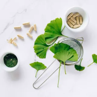 Ginkgo leaves, capsules, and powder in bowls on a white surface.