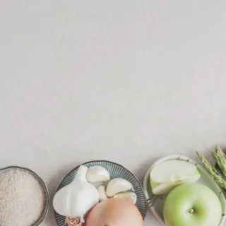 Assorted ingredients on plates: garlic, onion, apple, asparagus, oats, and rice on a light background.