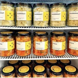 Jars of sauerkraut and kimchi on fridge shelves with yellow labels.