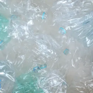 Crumpled clear plastic bottles with blue and green caps scattered on a surface.