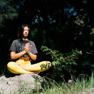 Person meditating outdoors on a rock, wearing yellow leggings and a dark T-shirt.
