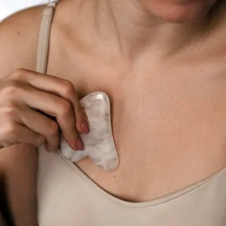 Person using a gua sha tool on chest in a beige top.