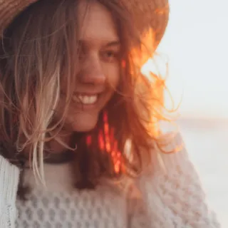 Woman in a straw hat smiling at sunset by the sea.