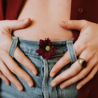 Hands on denim jeans with a red flower tucked in the waistband.